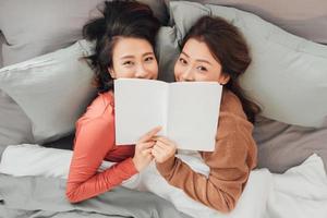 Two women lying on bed and reading book photo