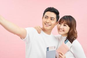 happy asian man and woman holding passports and air tickets while looking at camera isolated on pink photo