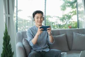 Young man leaning on sofa and playing games on phone at home photo