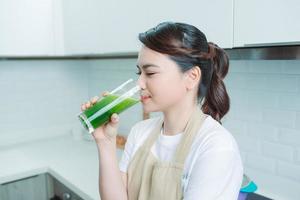 mujer bebiendo jugo de desintoxicación verde, bebida de batido en el retrato de la cocina. foto