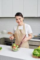 Beautiful young woman is preparing vegetable salad in the kitchen photo