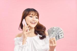 Image of a shocked surprised screaming young pretty woman posing isolated over pink wall background using mobile phone holding money. photo