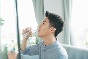 Single man drinking water from a glass sitting on a couch at home photo