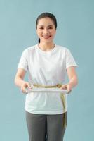 A asian woman holding scales with a tape measure around her belly on a blue background photo