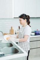 mujer joven con delantal lavando platos en la cocina moderna foto