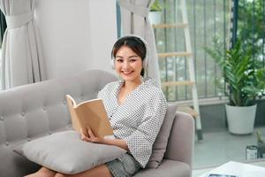 Young relaxed woman on sofa with headphones reading a book photo