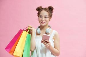 happy woman using smartphone and holding shopping bags isolated on pink photo