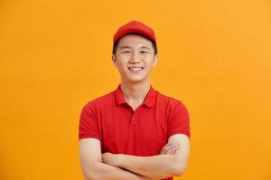 Smiling delivery man in red uniform standing with arm crossed - isolated on white background photo