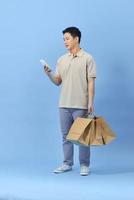 Young Asian man with shopping bags is using a mobile phone and smiling while doing shopping on blue background photo