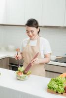 Young woman mixing fresh salad standing near desk photo