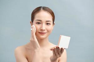 Charming woman applying powder on her face with cosmetic application. photo