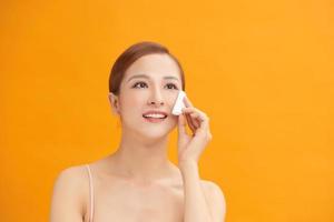 Beautiful woman removing her makeup using a cotton round  over a white background photo