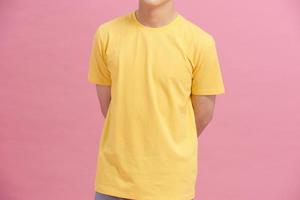 partial view of man in yellow t-shirt holding hands behind back isolated on pink photo