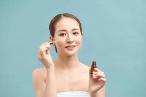 portrait of young woman applying serum on her face on violet background photo