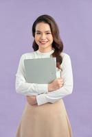 Happy beautiful young business woman standing and holding clipboard over purple background photo