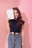 retrato joven mujer asiática feliz libro cubriendo su ojo sonriendo emoción positiva sobre fondo rosa foto