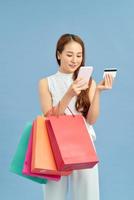 Stylish woman with shopping bag, credit card and phone on the blue wall background. Winter holiday sale photo