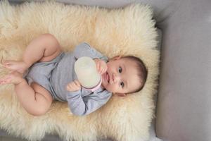 Baby girl holding and feeding milk from bottle lying on sofa. photo