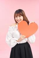 Cute asian woman holding red heart isolated on pink photo