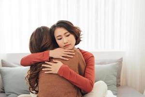 vista lateral de dos tristes buenos amigos abrazándose en un dormitorio en el interior de una casa foto