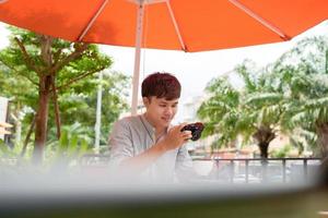 Smiling young male sitting at table in cafe with photo camera while drinking cup of coffee