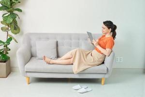 Beautiful young woman using tablet sitting on sofa at home at living room. photo