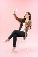 Smiling young woman making selfie photo on smartphone over pink background