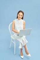 Fashionable young girl sitting on a chair with laptop isolated on blue background photo