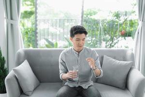 A handsome boy holds a transparent capsule, pills or vitamins and looks at it. photo