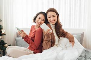 Smiling Two Asian young lovely couple repose on white bed and happy playing with smartphone and social media. photo