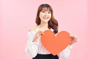 Image of gorgeous lady holding heart shaped paper against pink background photo