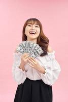 imagen de una mujer encantada vistiendo ropa básica sonriendo y sosteniendo dinero en efectivo aislado sobre fondo rosa foto
