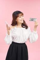 Portrait of happy joyous female 30s demonstrating lots of money dollar currency while using her mobile phone isolated over pink background photo