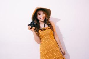 retrato de una joven sonriente con sombrero con una cámara posando aislada en un fondo pastel foto