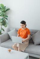 mujer sonriente sentada en un sofá relajándose mientras navega por el sitio web de compras en línea. foto