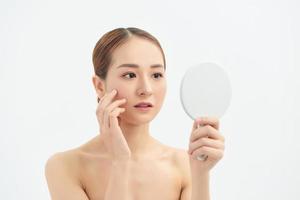 Young Asian woman with problem face looking at the mirror  over white background. photo