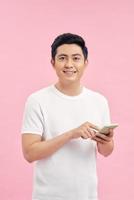 Smiling young good looking Asian man using smartphone to get in touch with family and friends isolated on bright pinkstudio background photo