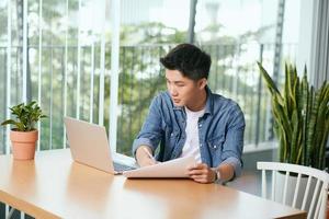 Rear view of a journalist stylish guy writing a story in a workplace in loft styled coworking, well dressed, sitting near window with view of garden photo