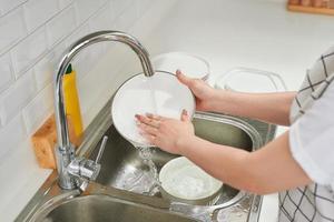 manos de mujer enjuagando platos con agua corriente en el fregadero foto