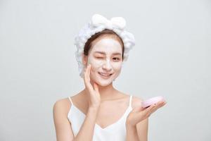 Beautiful young woman with towel wrapped around her head applying face mask photo