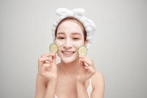 Young woman with clay facial mask holding cucumber slices isolated on white background photo