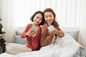 Young happy lesbian lgbtq couple or friends holding smartphone using mobile phone at home photo