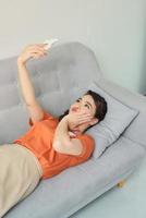 Beautiful young woman making selfie by smart phone while lying on couch at home photo