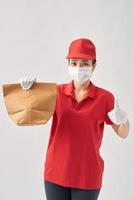 Delivery woman wearing coronavirus protection mask and holding paper bag over white photo