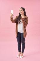 Portrait of an attractive young asian woman using mobile phone while standing with copy space over pink background photo