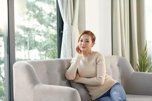 Young asian woman sitting on couch and dreaming on sofa at home photo