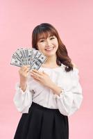 Picture of smiling young asian woman standing isolated over pink background. Looking camera holding money. photo