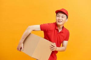 Cheerful delivery man. Happy young courier holding a cardboard box and smiling while standing against white background photo