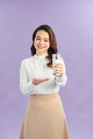 mujer sonriente sosteniendo un vaso de leche contra un fondo morado foto