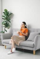 Serene young woman resting on sofa wearing casual home clothes wireless headphones enjoy weekend free time photo